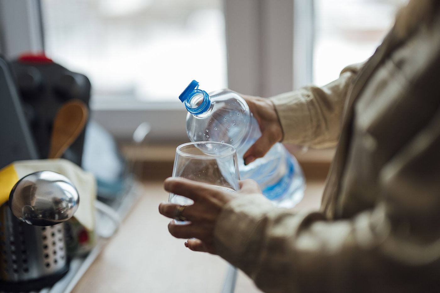 Person pours water from a bottle into a glass in a kitchen