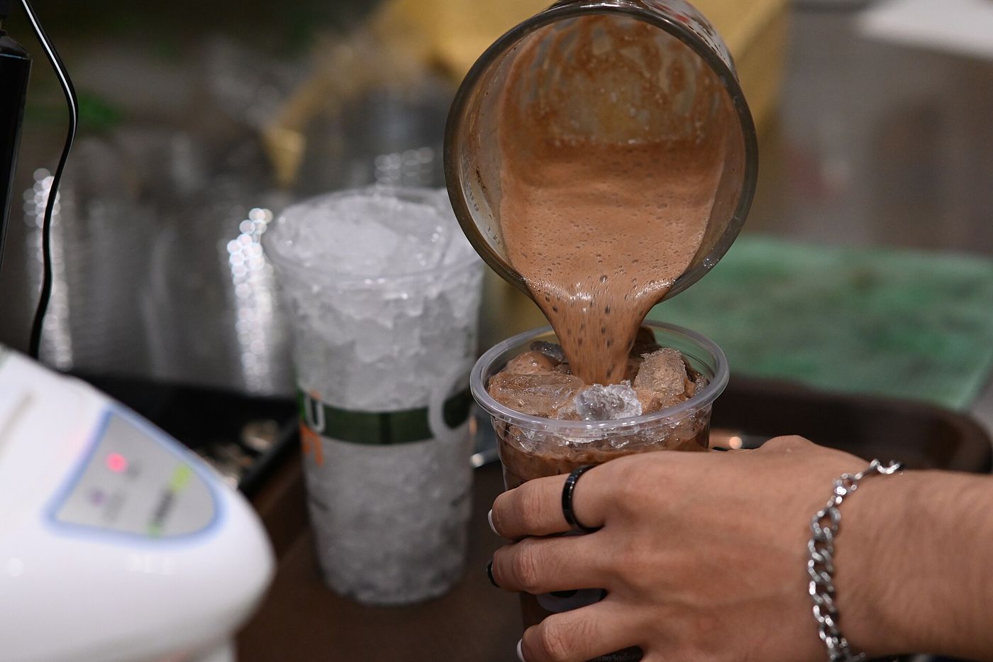 DFC 0816 A close-up of a hand holding a plastic cup while a chocolatey smoothie is poured over ice from a blender