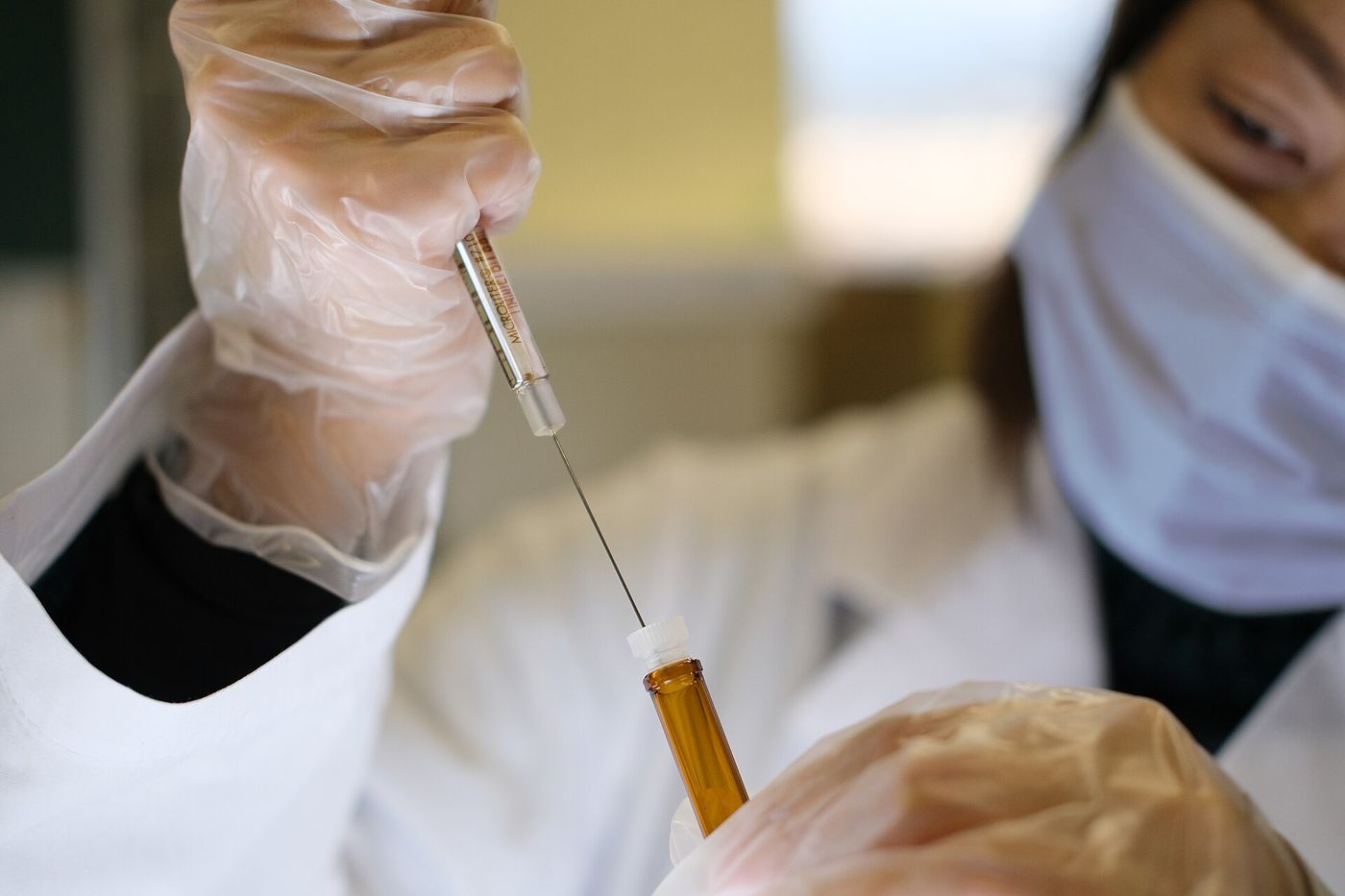 Japanese female scientist wearing plastic gloves holding syringe and vial, researching a coronavirus vaccine