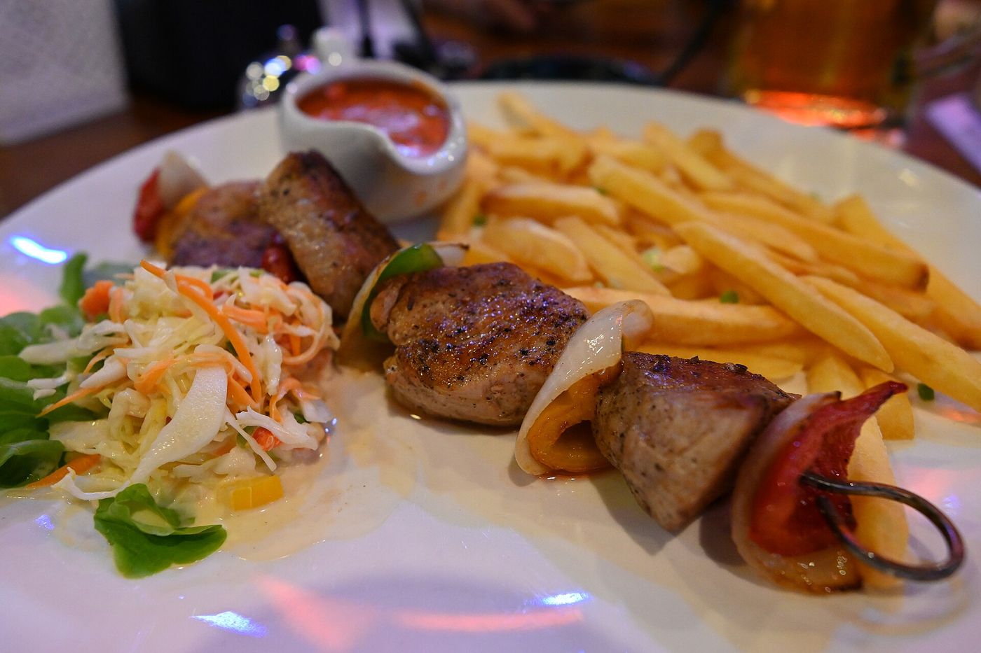 DFC 1025 A plate of grilled sausage skewers with roasted vegetables golden fries and a side of coleslaw with dipping sau